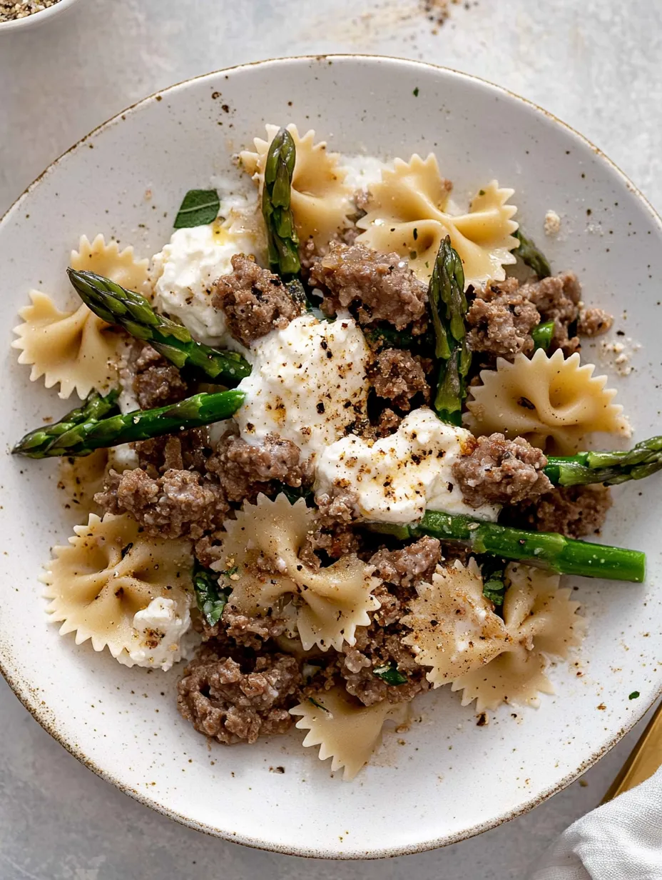A plate of food with pasta, sausage, and asparagus.