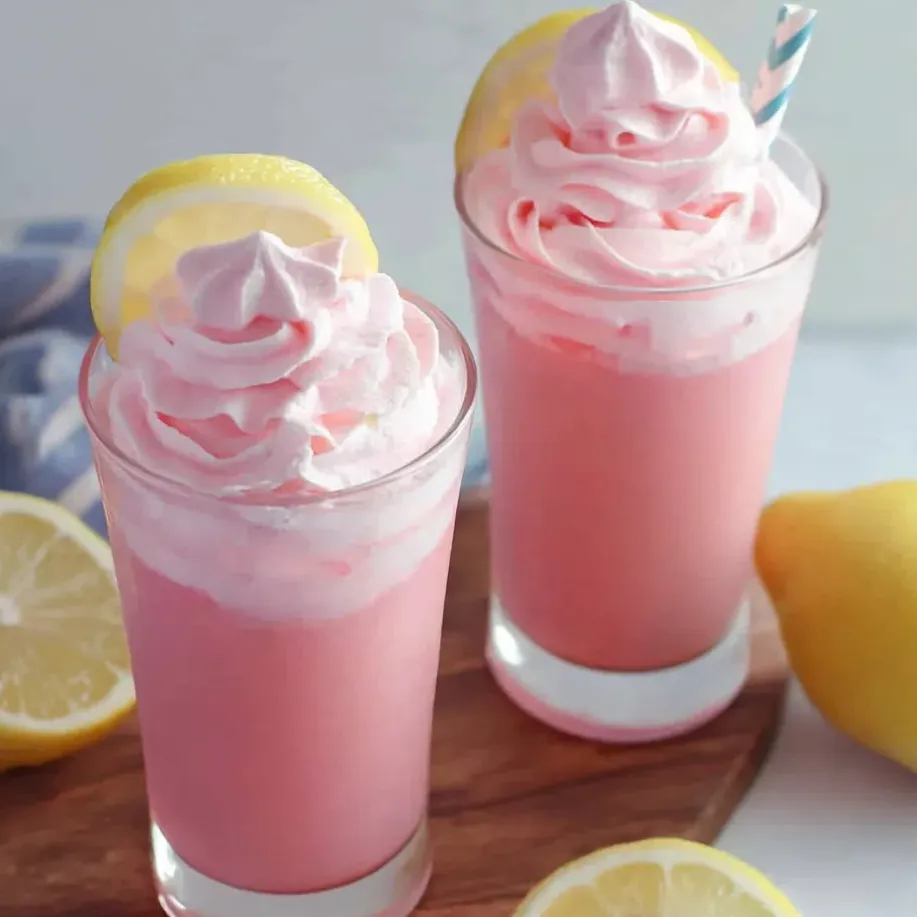 Two glasses of pink lemonade sitting on a table, each garnished with lemon slices.