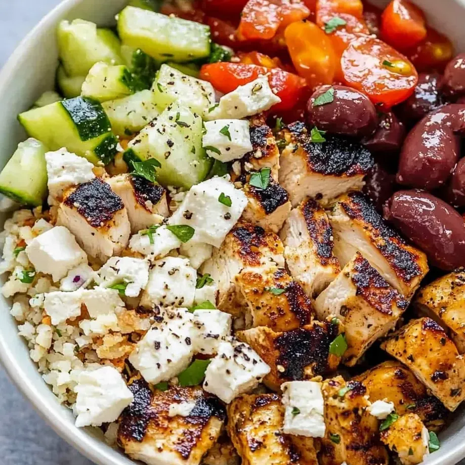 Bowl filled with chicken, cucumber, tomatoes, and olives ready to eat.