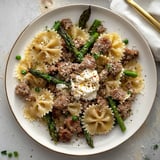 A plate of food with pasta, sausage, and asparagus.