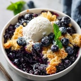 Blueberries in a bowl topped with ice cream.