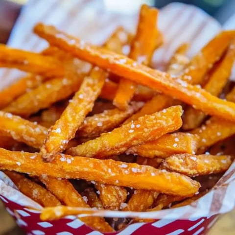 A basket stuffed with sweet potato fries on a red and white checked liner.