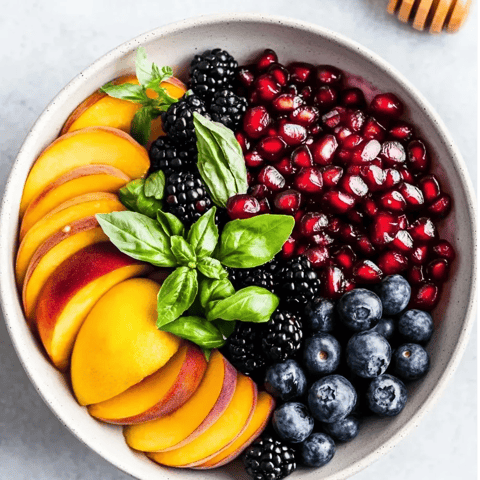 A bowl packed with blackberries, blueberries, peaches, and a drizzle of honey.