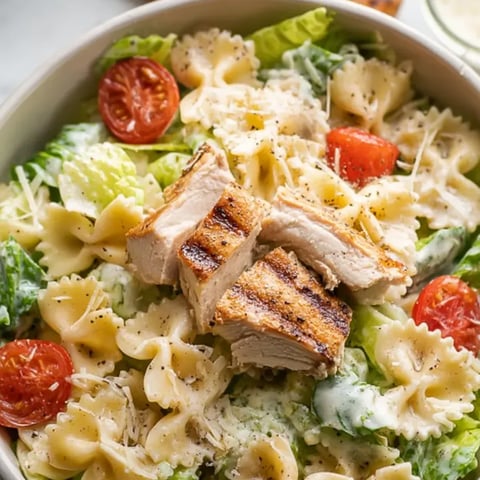 Pasta salad with chicken chunks and tomatoes in a bowl.